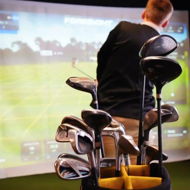 A set of golf clubs in a virtual golf simulator. Man practicing golf indoors.