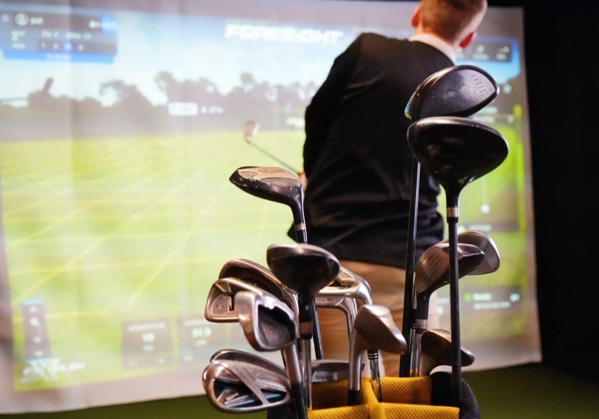A set of golf clubs in a virtual golf simulator. Man practicing golf indoors.