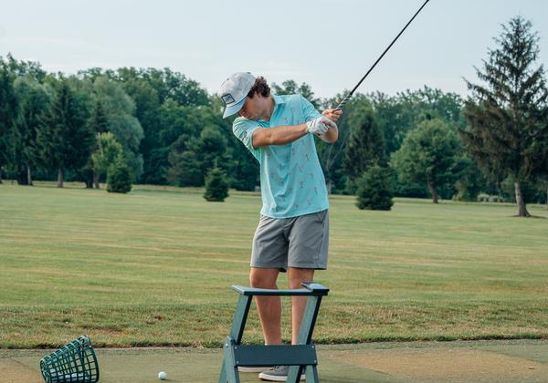 Man in golf attire swinging club on grassy course